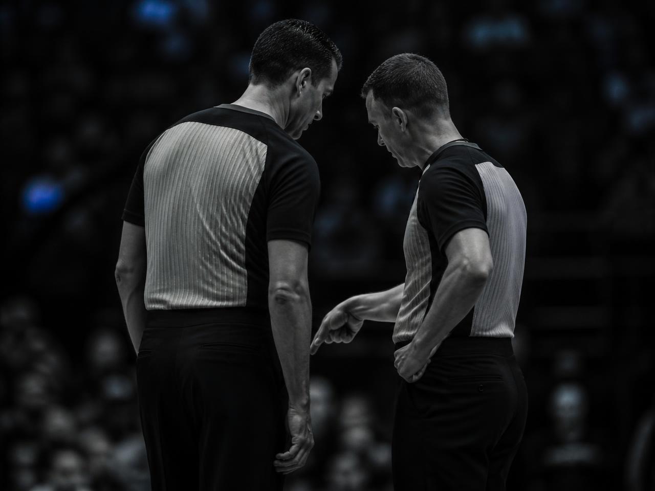 Two basketball officials talking calmly with each other courtside during a stoppage.
